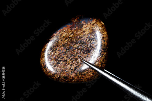 Bronzite jewel stone texture in tweezers on black background. Macro closeup. photo