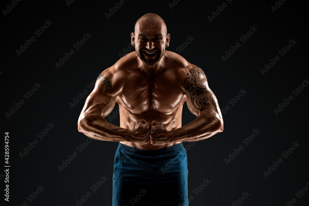 Tattooed male bodybuilder posing over black background. Fitness workout concept, muscle groups, watch your body.