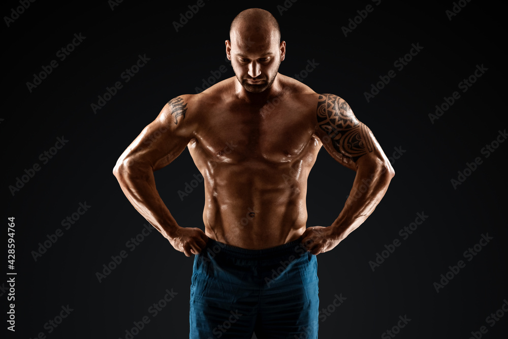 Tattooed male bodybuilder posing over black background. Fitness workout concept, muscle groups, watch your body.