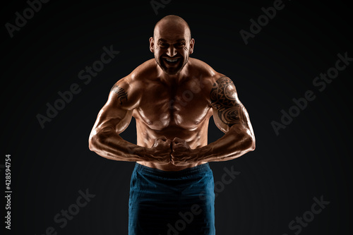 Tattooed male bodybuilder posing over black background. Fitness workout concept, muscle groups, watch your body. © Aliaksandr Marko