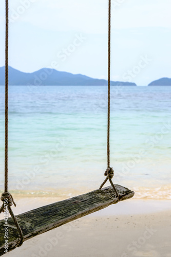 Close up, old swing hanging on a tree on sandy beach, blue sea and sky background.