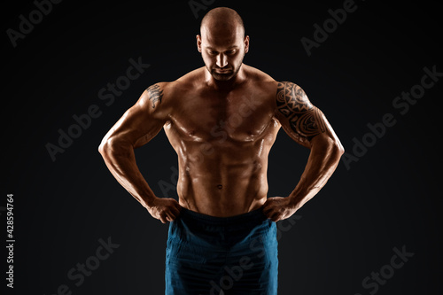 Tattooed male bodybuilder posing over black background. Fitness workout concept, muscle groups, watch your body.