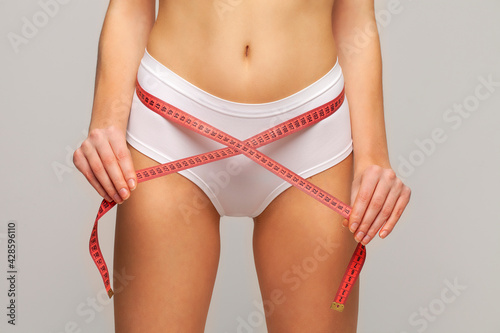 Slim young woman measuring her body with white metric tape measure after a diet