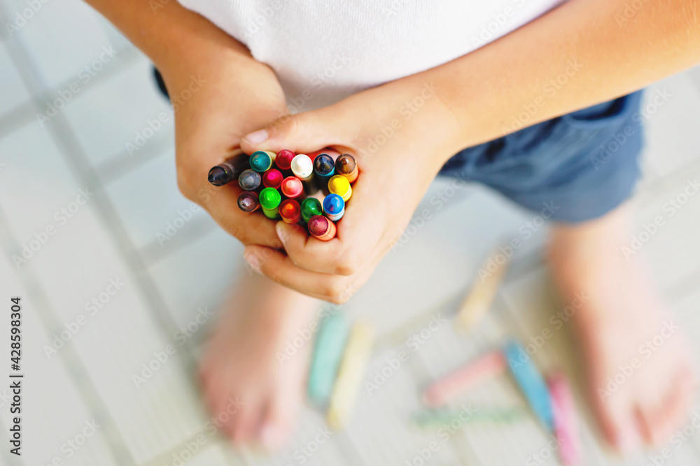 Close-up of child's hands with lots of colorful wax crayons pencils. Kid preparing school and nursery equipment and student stuff. Back to school. Education, school, learning concept