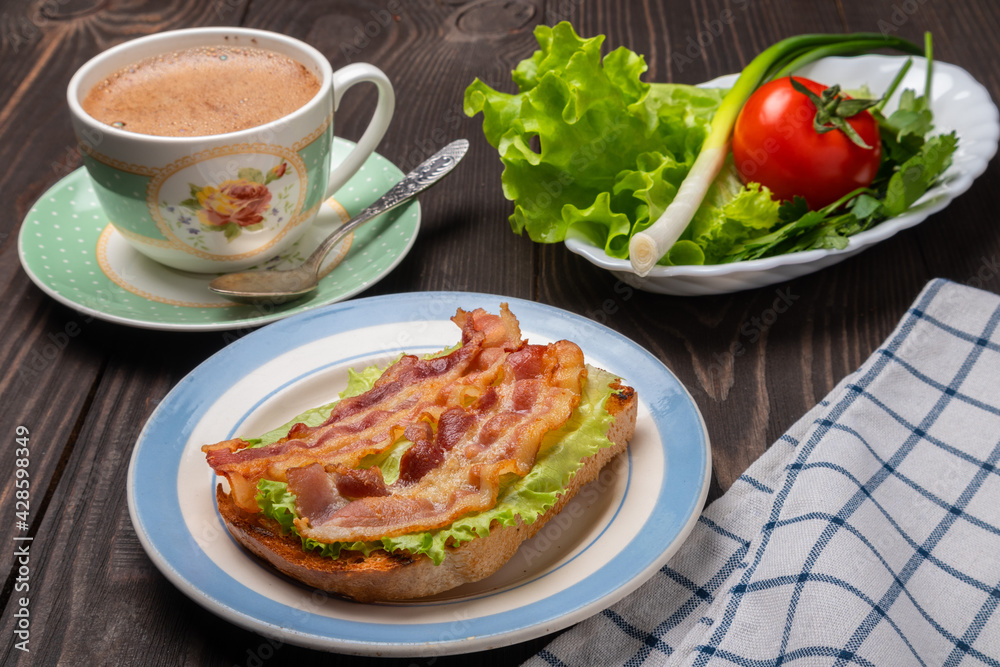sandwich with fried bacon on a lettuce leaf and a cup of coffee sandwich with fried bacon on a lettuce leaf and a cup of coffee