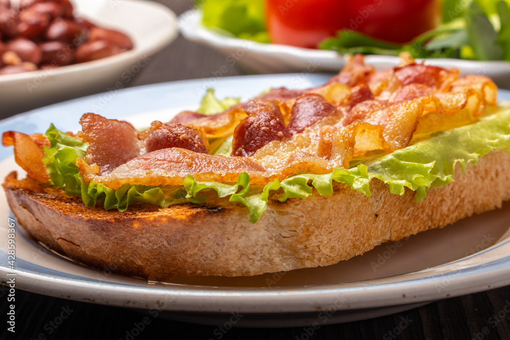 sandwich with fried bacon on a lettuce leaf closeup	
