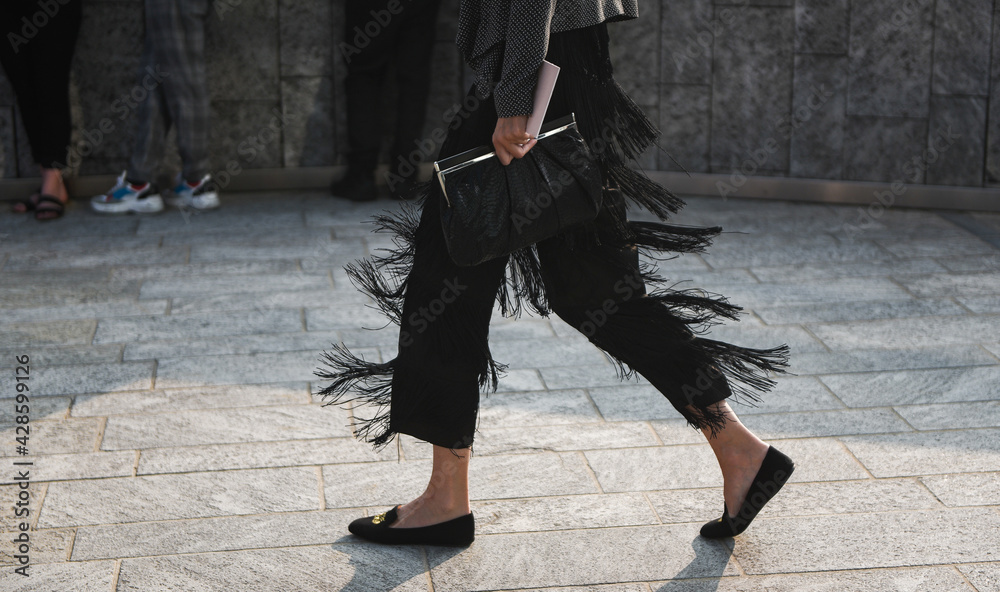 Fototapeta premium Detail of a fashionable outfit – woman wearing black pants with fringes and summer shoes