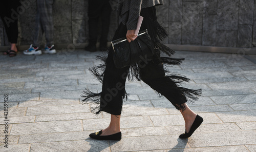 Detail of a fashionable outfit – woman wearing black pants with fringes and summer shoes