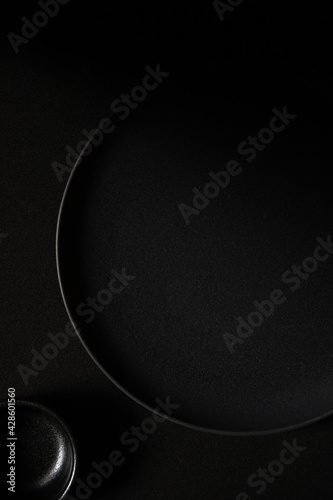 Black matt dish on a dark background with part of a little bowl.