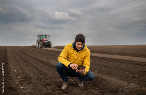 Farmer with tablet in front of tractor in field