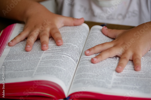 Uma criança com sua mão em cima da biblia na mesa pronta para rezar com letras pequenas e desfocada. photo