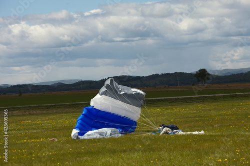Skydiver lies on a green field trying to extinguish a filled parachute canopy after a hard landing.