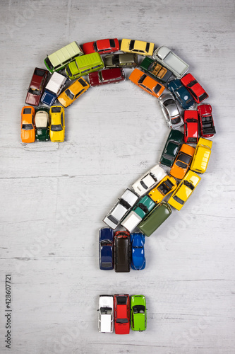 question mark, formed with toy cars, on a gray wooden board