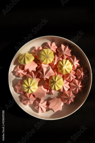 pink and yellow meringue in white dish on a black background with sunlight
