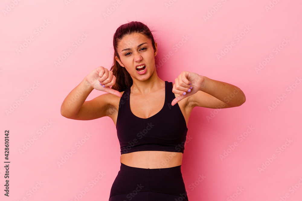 Young sport Indian woman isolated on pink background showing thumb down and expressing dislike. Young sport Indian woman isolated on pink background showing thumb down and expressing dislike.