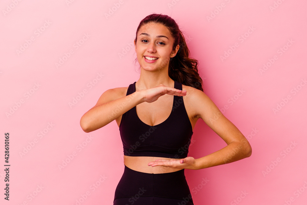 Young sport Indian woman isolated on pink background holding something with both hands, product presentation. Young sport Indian woman isolated on pink background holding something with both hands, product presentation.