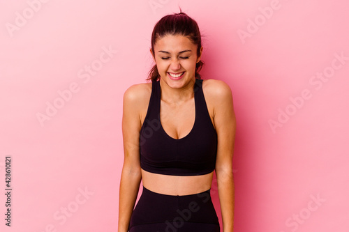 Young sport Indian woman isolated on pink background laughs and closes eyes, feels relaxed and happy. © Asier