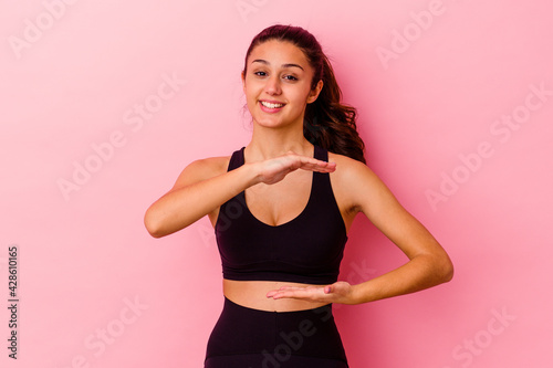 Young sport Indian woman isolated on pink background holding something with both hands, product presentation. © Asier