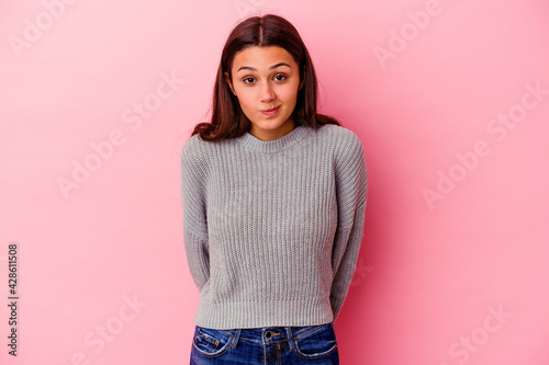 Young Indian woman isolated on pink background shrugs shoulders and open eyes confused.