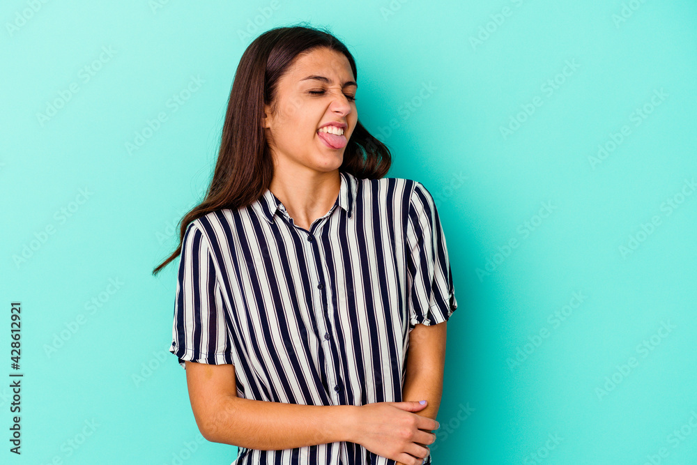 Young Indian woman isolated on blue background funny and friendly sticking out tongue. Young Indian woman isolated on blue background funny and friendly sticking out tongue.