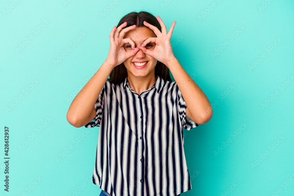 Young Indian woman isolated on blue background excited keeping ok gesture on eye. Young Indian woman isolated on blue background excited keeping ok gesture on eye.