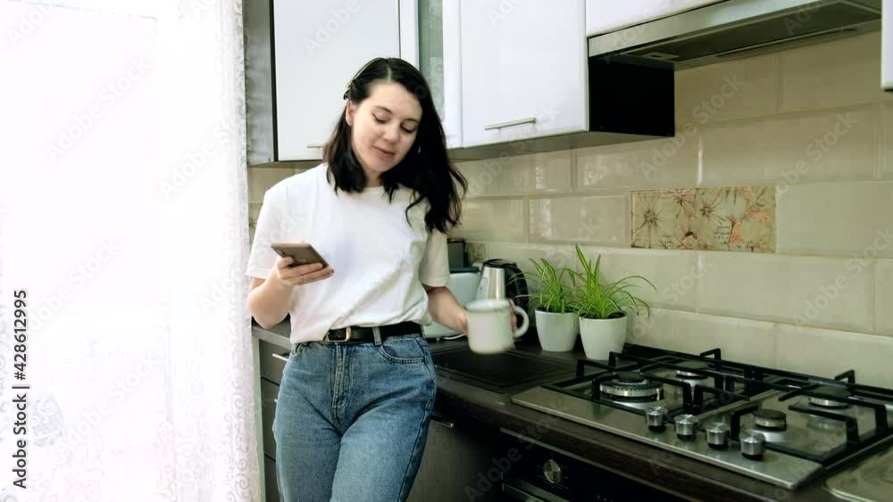 young woman drinking morning coffee at the kitchen checking news on the phone young woman drinking morning coffee at the kitchen checking news on the phone