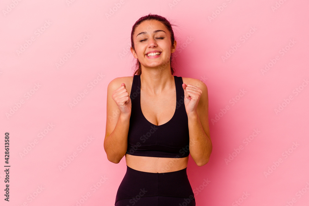 Young sport Indian woman isolated on pink background raising fist, feeling happy and successful. Victory concept. Young sport Indian woman isolated on pink background raising fist, feeling happy and successful. Victory concept.