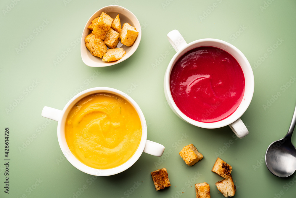 Vegetarian beetroot and pumpkin cream soups in a bowls with croutons on a green background, top view