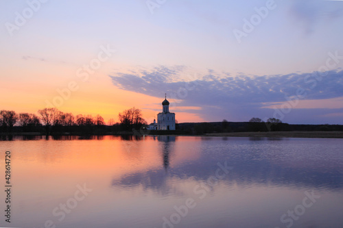 Watercolor dawn landscape in high water - with the silhouette of a church on the horizon and reflections on the surface of a meadow flooded with melting snow.
