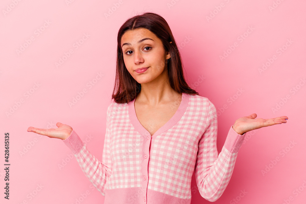 Young Indian woman isolated on pink background confused and doubtful shrugging shoulders to hold a copy space. Young Indian woman isolated on pink background confused and doubtful shrugging shoulders to hold a copy space.