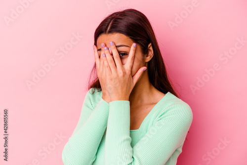 Young Indian woman isolated on pink background blink through fingers frightened and nervous. © Asier