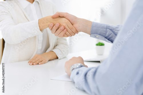 Casual dressed businessman and woman shaking hands after contract signing in white colored office. Handshake concept
