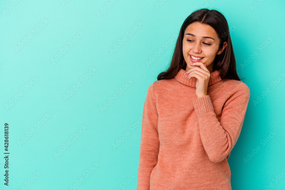 Young Indian woman isolated on blue background relaxed thinking about something looking at a copy space. Young Indian woman isolated on blue background relaxed thinking about something looking at a copy space.