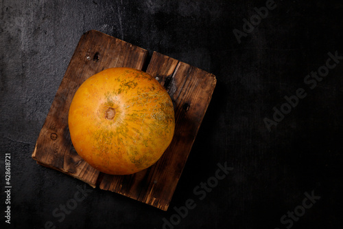 Sweet ripe yellow melon on kitchen board, black background. Organic seasonal farm fruits concept. Healthy vegan food. Copy space.