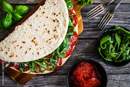 Italian piada wraps - piadina stuffed with fresh vegetable leaves and salami sausage on wooden table
 photo