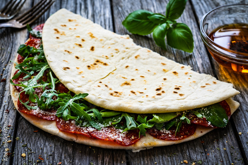 Italian piada wraps - piadina stuffed with fresh vegetable leaves and salami sausage on wooden table
