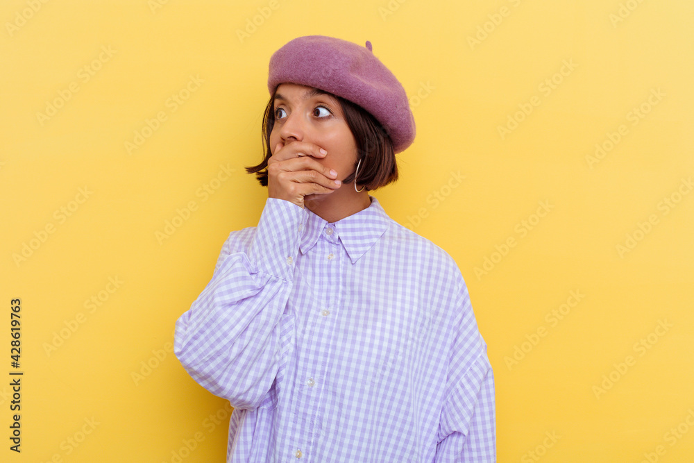 Young mixed race woman wearing a beret isolated on yellow background thoughtful looking to a copy space covering mouth with hand. Young mixed race woman wearing a beret isolated on yellow background thoughtful looking to a copy space covering mouth with hand.