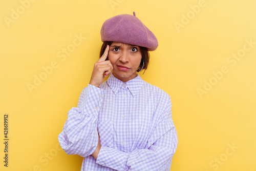Young mixed race woman wearing a beret isolated on yellow background focused on a task, keeping forefingers pointing head.