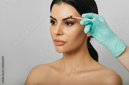 Botulinum toxin injections near a woman's forehead for blocking mimic wrinkles and wrinkles removal. Beautiful female face, close-up on grey background