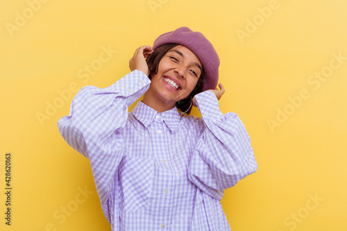 Young mixed race woman wearing a beret isolated on yellow background laughs joyfully keeping hands on head. Happiness concept. © Asier