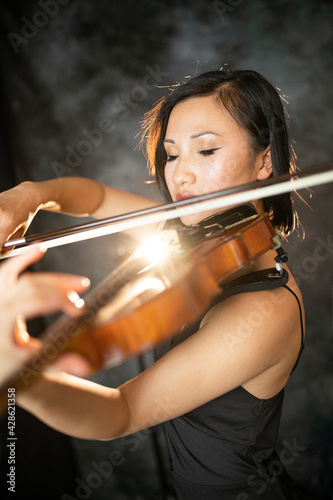 An Asian young woman is playing violin. Violinist is performing on the stage. 