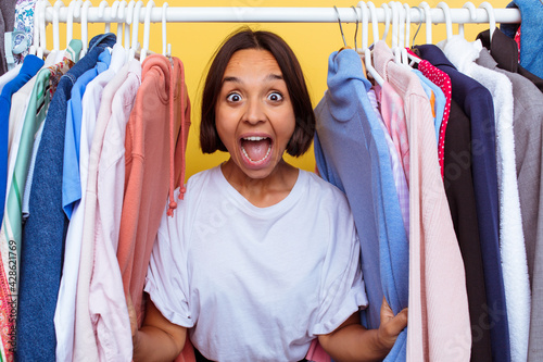 Young girl coming out of a coat rack isolated on yellow background