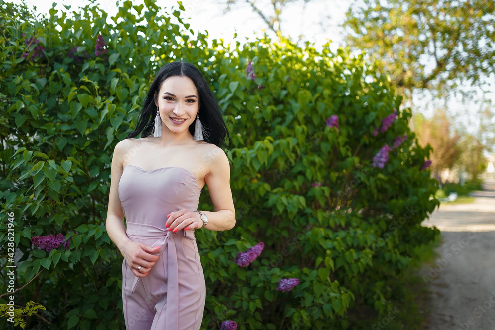 Portrait of young pretty woman with dark long hair among blossoming lilac bushes in spring. Portrait of young pretty woman with dark long hair among blossoming lilac bushes in spring.