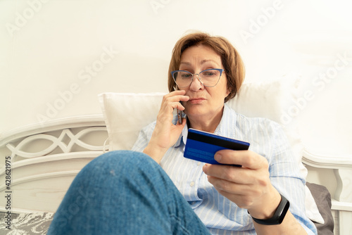 Elderly woman frustratedly talking on a mobile phone and holding a bank card in her hand