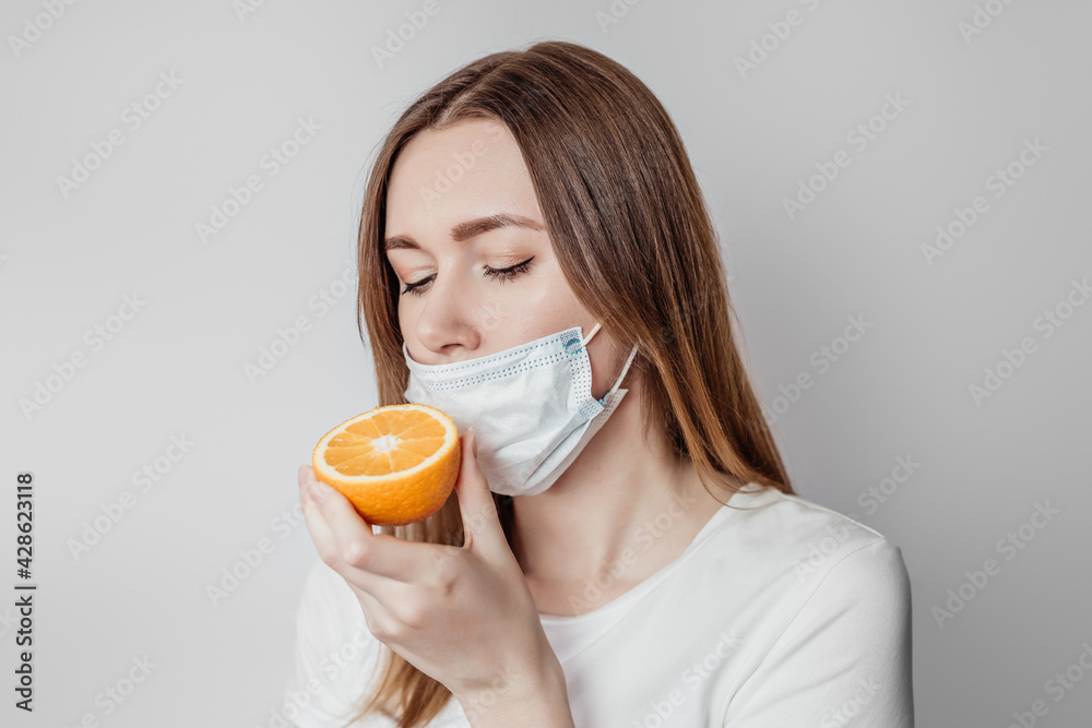 Loss of smell concept. Caucasian young woman in a medical mask sniffing an orange on a white background in the studio Loss of smell concept. Caucasian young woman in a medical mask sniffing an orange on a white background in the studio