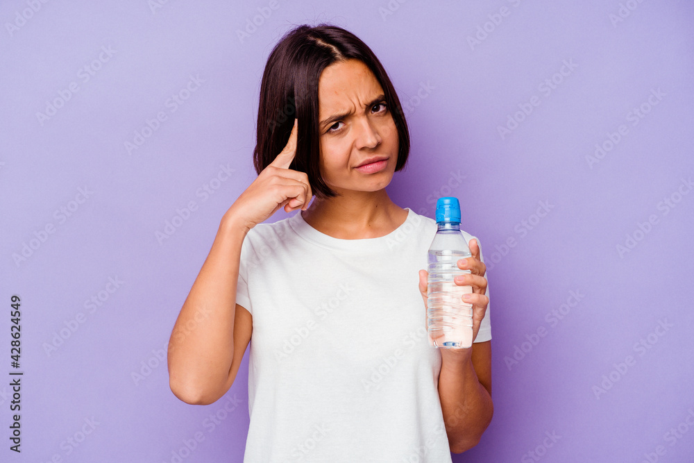Young mixed race holding a water bottle isolated on purple background pointing temple with finger, thinking, focused on a task. Young mixed race holding a water bottle isolated on purple background pointing temple with finger, thinking, focused on a task.