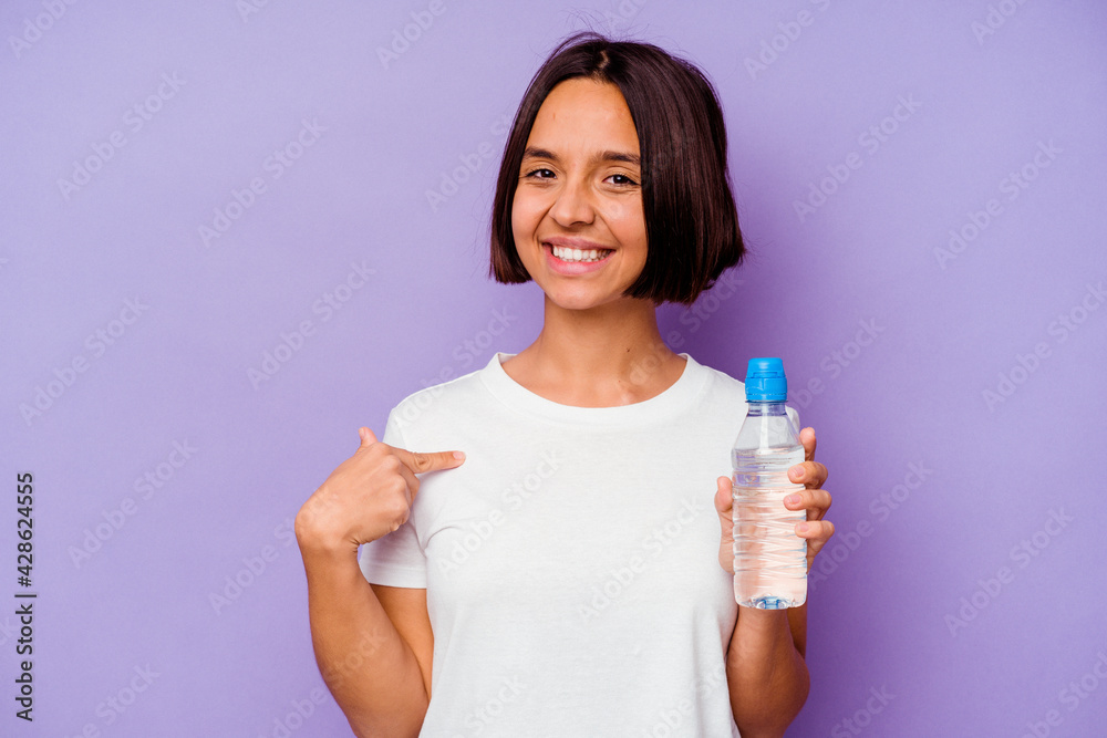 Young mixed race holding a water bottle isolated on purple background person pointing by hand to a shirt copy space, proud and confident Young mixed race holding a water bottle isolated on purple background person pointing by hand to a shirt copy space, proud and confident