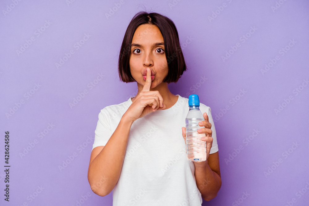 Young mixed race holding a water bottle isolated on purple background keeping a secret or asking for silence. Young mixed race holding a water bottle isolated on purple background keeping a secret or asking for silence.
