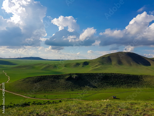 A panoramic view on a hilly landscape of Xilinhot in Inner Mongolia. Endless grassland with a few wind turbines between. Blue sky with thick, white clouds. A small gravel road through the pasture. photo