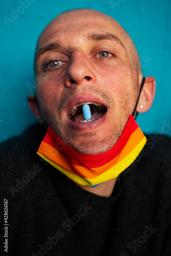 Adult Caucasian gay man holding a blue PrEP (pre-exposure prophylaxis) drug pill in open mouth; HIV prevention concept